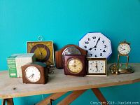 View of all eight clocks arranged on a wooden table showing different styles, including wood-cased and boxed clocks.