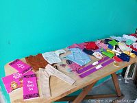 Wide angle view of assorted doll clothes spread out on table, showing variety and quantity