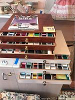 Brown wood-finish chest with three drawers open showing various colored thread spools