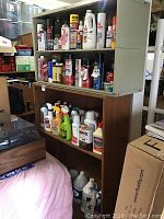 Wide angle view of shelving units filled with assorted household and automotive chemical products in spray bottles, cans, and jugs.