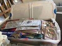 Open plastic underbed container filled with various paper crafting supplies and kits, papers visible inside