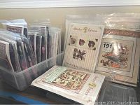 Assortment of sealed quilt kit packets in a plastic bin and on tabletop, including P3 Designs and Shabby Fabrics series.