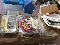 Photo showing multiple embroidery hoops in wooden, pink, and blue varieties stacked inside plastic containers with other sewing supplies.