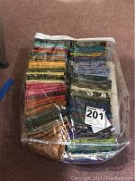 Full view of the fabric collection folded and organized inside a transparent zippered plastic bag on carpeted floor, showing variety of colors and patterns.