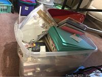 Plastic container filled with various crafting paper supplies and paper packs in original shrink wrap packaging.