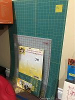 Large and medium green cutting mats with grid lines leaning against wall, Omnigrid and OLFA kits in front.