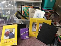 Overview of sketch pads including several Strathmore Bristol vellum pads with yellow covers, a small purple watercolor pad, black bound journal, plus visible calligraphy and drawing papers all arranged on floor next to lidded plastic storage container.
