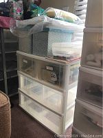 White plastic three-drawer storage container with floral and pink decorative boxes on and around it.