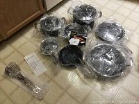 Photo showing all 14 pieces of the cookware set including pans, pots, lids, utensils, and packaging with informational inserts.