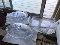 Two glass oval covered casserole dishes with embossed designs and two rectangular glass baking dishes on paper towels.
