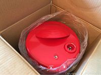 Red pressure cooker lid with pressure valve inside a box.