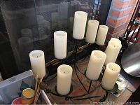 10 candle black metal LED candelabra holding white flameless pillar candles in varying heights placed on brick hearth in front of fireplace.