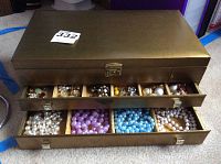 Metal jewelry chest with upper compartments holding earrings, pins and colorful costume jewelry pieces.