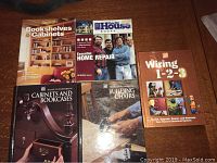 Front covers of five books on home repair, woodworking, and electrical wiring laid out on a table.