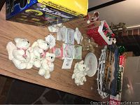 Lot of Christmas decor items on wooden table including collectible figurines, ornaments, Christmas plate, and boxed laser light