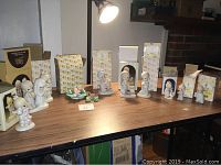 Wide shot of all Precious Moments figurines lined up on a table, some in original boxes behind figurines.