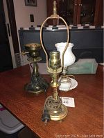 Three old electric lamps on a table. The milk glass lamp with white glass shade and base plate is in the middle, with two brass and copper finish lamps on either side. Visible wiring shows signs of old age.