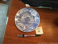 Top view of blue and white souvenir plate with New York World's Fair scenes and a stainless steel letter opener below it on wood surface.