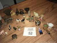 Photo showing various miniature figurines and collectibles spread on a wooden table including brass candlesticks, pewter animals, miniature irons, glass bottles, and various small animal figures.