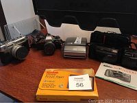 Yashica Electra 35 camera, Olympus OM10, Nikon cameras and Kodak paper displayed on a table