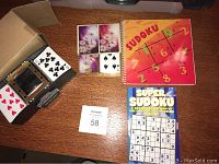 Overview of all items on table including two decks of cards, two Sudoku books, and the card shuffler.