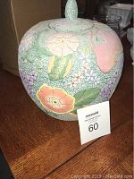 Side view of the round ceramic decorative jar showing pastel floral relief design with crackled texture and lid finial