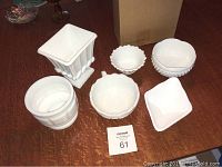 Six white milk glass pieces arranged on a table, showing the collection and relative sizes of planters, bowls, and a handled bowl.