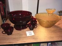 Ruby glass punch bowl with stand and six matching punch glasses, and amber chip and dip bowl on wooden surface.