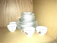 Stacked good condition Limoges china plates, cups, and bowls inside wooden cabinet.