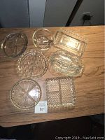 Top down view of all seven small glass serving dishes arranged on a wooden table showing various shapes and divided sections.