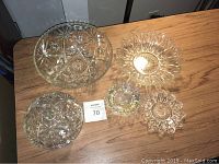 Overview photo of all glass pieces on wooden surface showing large bowl, covered dish with lid, and four shallow dishes with starburst patterns.