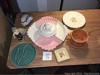 Photo showing all ceramic items arranged on table including divided serving set with covered center, deviled egg dish, carved trivet, figurine, planter mug, basket dish, and tea trivet.