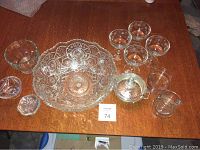 Photo showing the entire set of glass items including large bowl, small bowls, wine glasses, server with lid and metal trivet, and floral frogs on a wood table.