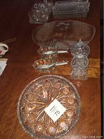 Top view showing multiple glass serving items including trays, sugar bowl, creamer, silverware holders, and drinking glasses arranged on a wooden table