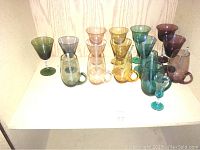 Photo of colored drinkware including various colored glasses and mugs arranged on a shelf.