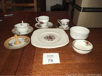 Photo showing nine total items: a small floral hand painted dish, a wooden handled item, two tea cups with saucers, two small decorated bowls, a Conway Wedgwood square plate, and smaller floral tea cup and saucer