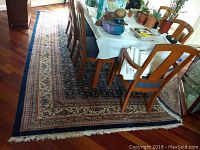 Full view of large rug placed under dining table on hardwood floor, showing pattern and fringe edges.
