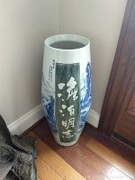 Tall ceramic vase with blue landscape painting and Chinese calligraphy from front angle near corner.