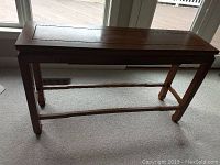 Front view of the rectangular sofa table showing the carved apron and stretcher support.