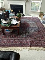 Full view of red-based handwoven rug laid in living room with coffee table, showing overall pattern and fringe ends