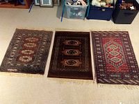 Three Pakistani carpets laid side by side on carpeted floor showing front surface and fringe edges.
