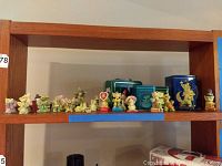Multiple figurines and tins on wooden shelf, overview of lot