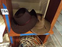 Two wide brim men's hats on wooden shelf, one tan and one dark brown.