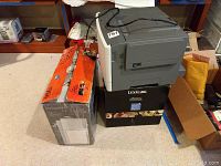 Overall view of the printers and boxes stacked on the floor, showing Lexmark printer on top of two boxes and Epson printer boxed on the side