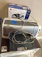 HP printer model C8954B with power and USB cables on table, showing front and top view of the printer.