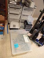 Two white Elfa rolling storage units with mesh drawers and hardtop surfaces, Ikea shoe rack, canvas cubbies and plastic containers arranged on carpeted floor.