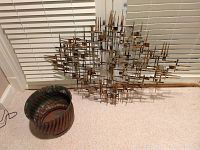 Metal 3D wall art and copper-colored metal gardening pot placed on carpet in front of window blinds.