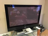 Samsung 42 inch plasma TV on a glass and metal stand showing front screen and remote control placed on the stand.