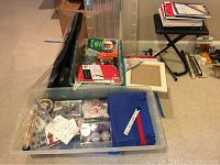 Photo showing plastic bin with assorted arts and crafts materials such as beads, spools of thread, small paint jars, assorted tools, and a white plastic frame.