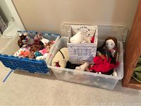Wide shot of two large plastic bins filled with assorted plush toys including Beanie Babies and a doll beside a doghouse shaped box.